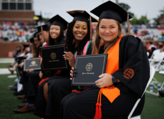 Mercer recognized for fostering student success from enrollment to post-graduation Mercer graduates in caps and gowns sit in rows holding diplomas during an outdoor graduation ceremony.