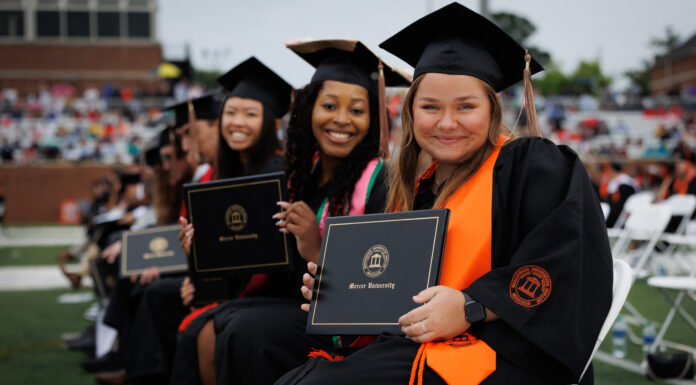 Mercer recognized for fostering student success from enrollment to post-graduation Mercer graduates in caps and gowns sit in rows holding diplomas during an outdoor graduation ceremony.