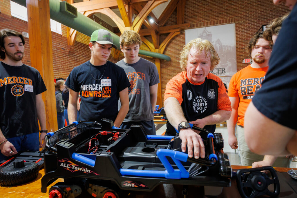 A group of students gathers as an instructor explains parts of a modified toy car.