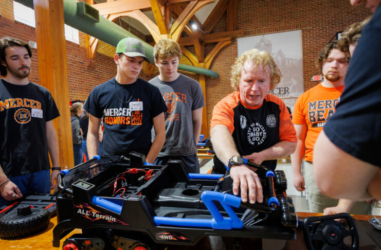A group of students gathers as an instructor explains parts of a modified toy car.