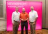 Auxiliary Services receives Illumia Distinction Award for Innovation Excellence Three men stand in front of a pink Momentum: An Illumia Experience sign, with one holding a clear award.