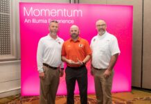 Auxiliary Services receives Illumia Distinction Award for Innovation Excellence Three men stand in front of a pink Momentum: An Illumia Experience sign, with one holding a clear award.