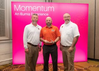Auxiliary Services receives Illumia Distinction Award for Innovation Excellence Three men stand in front of a pink Momentum: An Illumia Experience sign, with one holding a clear award.