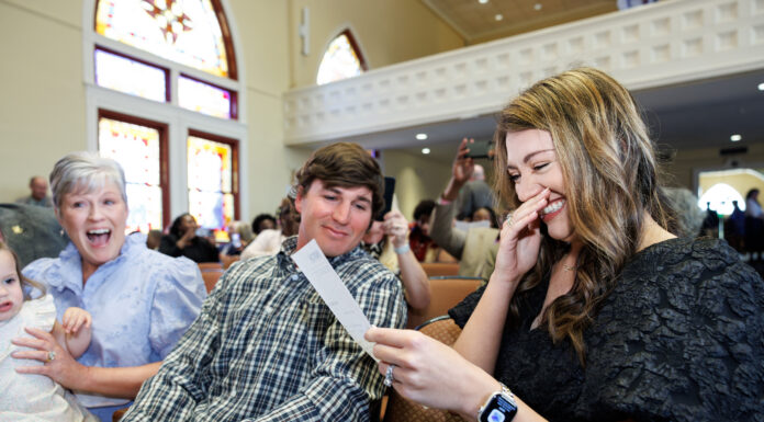 School of Medicine celebrates National Residency Match Day 2026 A young woman smiles and covers her mouth while reading a card, seated with two others in a church.