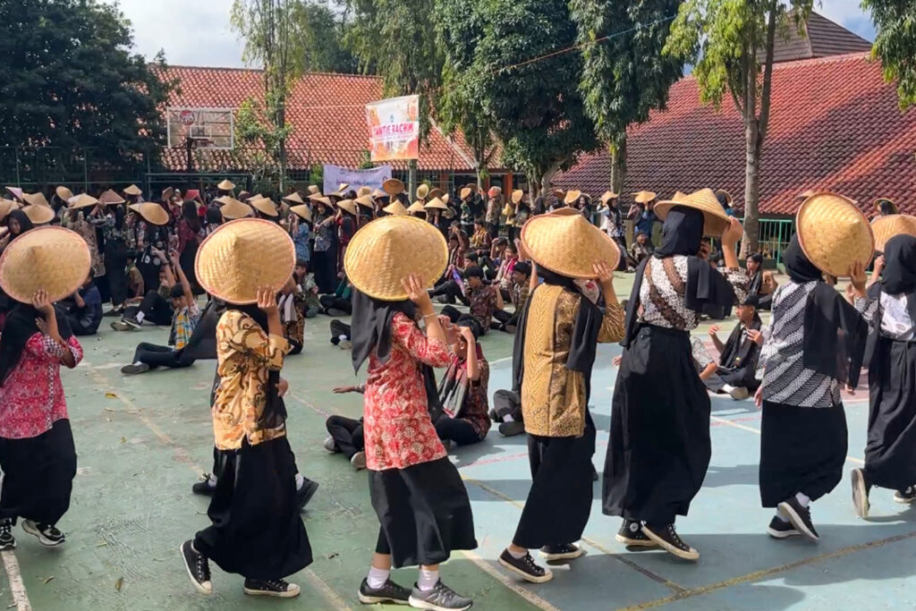 People in traditional attire and straw hats perform a group dance outdoors.
