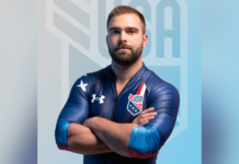 Mercerian competes in bobsled events in Winter Olympics A male athlete in a blue USA uniform stands with arms crossed in front of a blurred USA logo background.