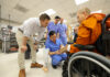 Mercer On Mission team fits monk injured in peace walk with prosthetic leg A group of medical professionals shows a prosthetic leg to a person in a wheelchair inside a lab.