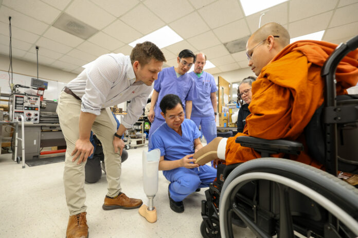 A group of medical professionals shows a prosthetic leg to a person in a wheelchair inside a lab.