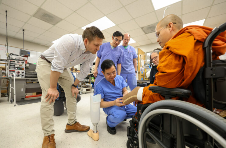 A group of medical professionals shows a prosthetic leg to a person in a wheelchair inside a lab.
