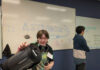 Mercer students, faculty bring space science to Girl Scouts Student holding a telescope in front of a whiteboard with ASTRONOMY and space-themed drawings; another student stands nearby.