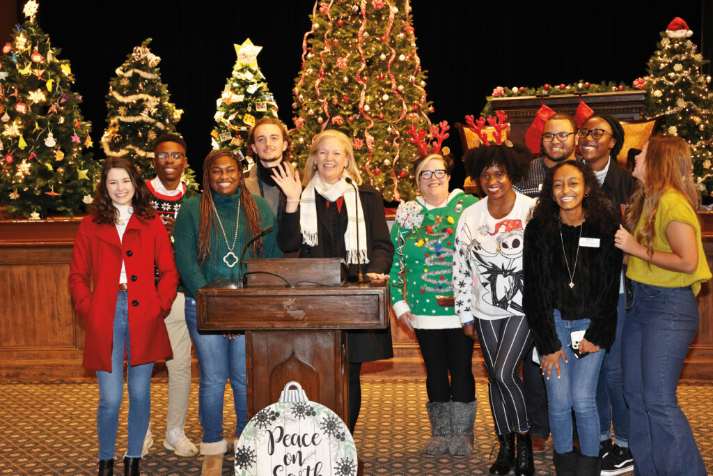 A group of people smiling and posing by a podium with Christmas trees and holiday decorations in the background.