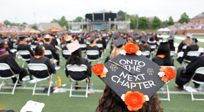 Mercer to confer degrees to more than 2,200 graduates at four commencements in May Graduate wearing a decorated cap reading Onto the Next Chapter at an outdoor commencement ceremony with seated attendees.