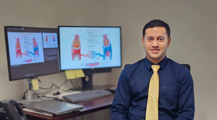 Mercer pharmacy professor named Fellow of the American Heart Association Man in business attire sits at a desk with documents, glasses, and two monitors displaying medical diagrams behind him.
