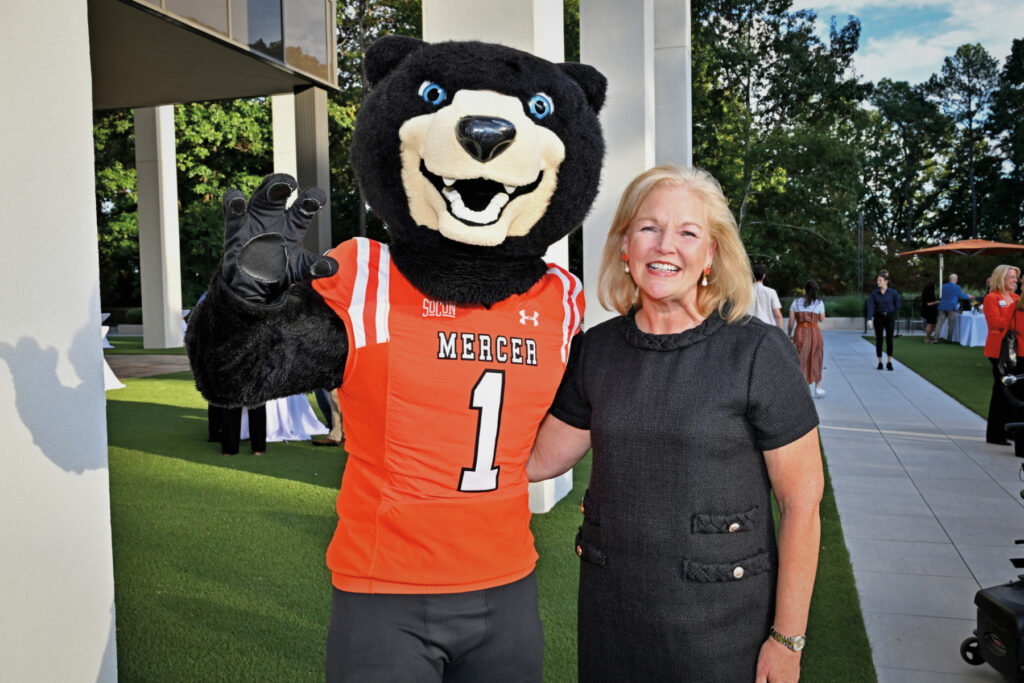 A woman stands smiling beside a person in a Mercer bear mascot costume outdoors at an event.