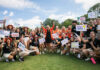 Mercer president proud to lead the university that changed her life A group of smiling young people, mostly in black shirts and khaki shorts, hold up signs with various names and drawings.