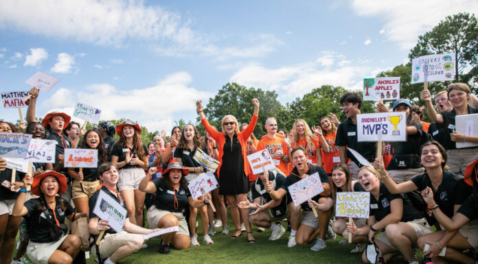 Mercer president proud to lead the university that changed her life A group of smiling young people, mostly in black shirts and khaki shorts, hold up signs with various names and drawings.