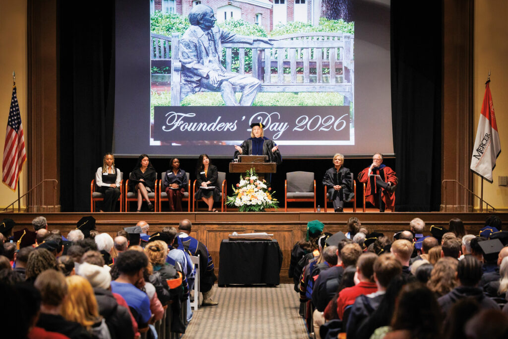 Mercer President Dr. Penny L. Elkins addresses an audience at a Founders Day 2026 event, with a statue image displayed behind the stage.