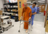 Pave a path to peace one step at a time | Dr. Craig McMahan A man wearing scrubs assists a monk with a prosthetic leg as he walks using a walker in a lab.
