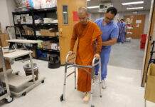 Pave a path to peace one step at a time | Dr. Craig McMahan A man wearing scrubs assists a monk with a prosthetic leg as he walks using a walker in a lab.