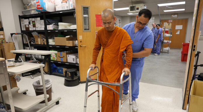 Pave a path to peace one step at a time | Dr. Craig McMahan A man wearing scrubs assists a monk with a prosthetic leg as he walks using a walker in a lab.