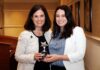 French professor forges new pathways for students Two women standing indoors, smiling and holding a star-shaped award together in front of a podium.
