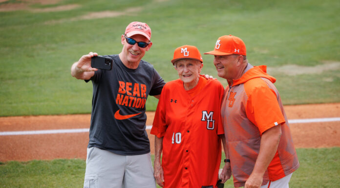 ‘Bloody Mary’ throws first pitch at Mercer baseball game Three people in Mercer University baseball attire pose for a selfie on a baseball field near the foul line.