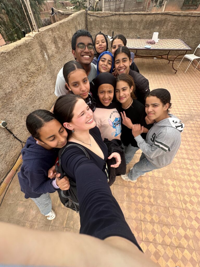 A group of smiling people pose closely together for a selfie on a tiled rooftop terrace.