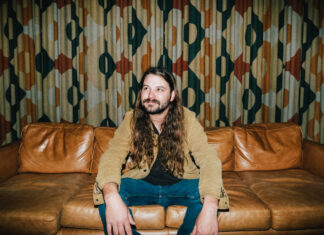 Brent Cobb hosts 2nd South of Atlanta Fest at Robins Financial Capitol Theatre Brent Cobb sits on a leather couch in front of patterned curtains.