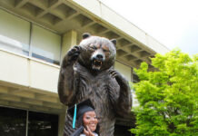Graduate Spotlight: Brittany Jones Brittany Jones in cap and gown poses in front of a large bear statue on a brick walkway outside a building.