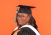 Graduate Spotlight: Charlotte Whitehead Charlotte Whitehead in graduation cap and gown with orange and white stoles, standing in front of an orange background.