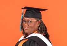 Graduate Spotlight: Charlotte Whitehead Charlotte Whitehead in graduation cap and gown with orange and white stoles, standing in front of an orange background.