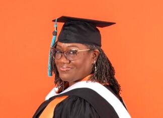 Graduate Spotlight: Charlotte Whitehead Charlotte Whitehead in graduation cap and gown with orange and white stoles, standing in front of an orange background.