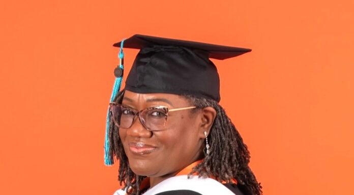 Graduate Spotlight: Charlotte Whitehead Charlotte Whitehead in graduation cap and gown with orange and white stoles, standing in front of an orange background.