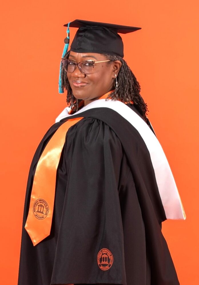 Charlotte Whitehead in graduation cap and gown with orange and white stoles, standing in front of an orange background.
