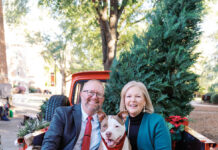 Meet Mercer’s new First Dog: Champ Jason Elkins and Mercer President Dr. Penny L. Elkins sit with a dog in the back of a red truck decorated with Christmas trees and blankets.