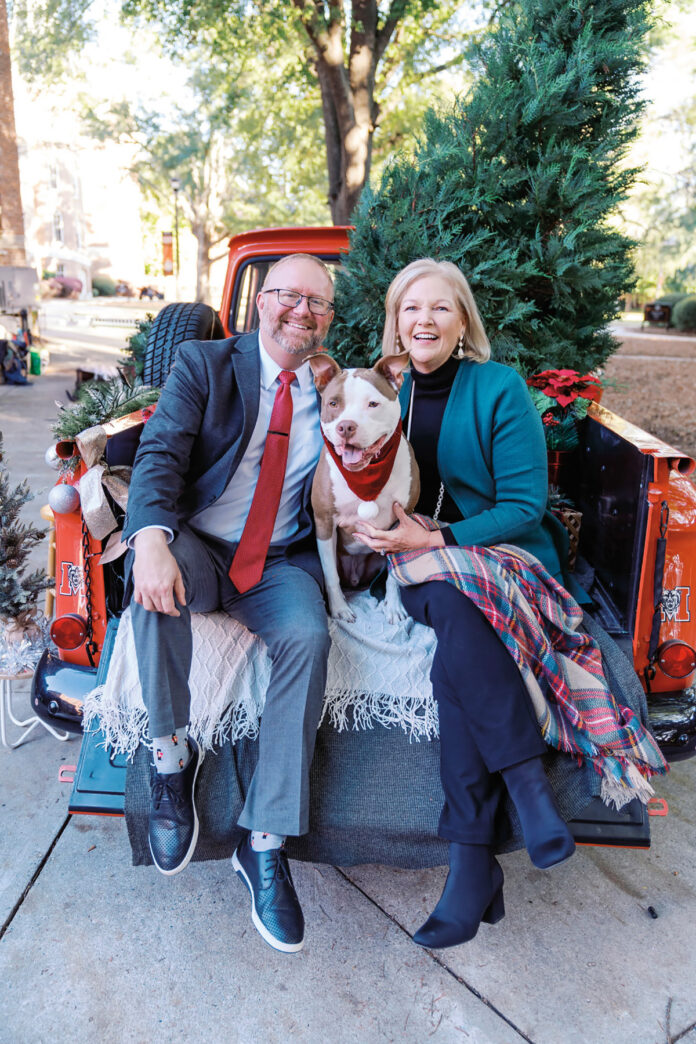 Jason Elkins and Mercer President Dr. Penny L. Elkins sit with a dog in the back of a red truck decorated with Christmas trees and blankets.