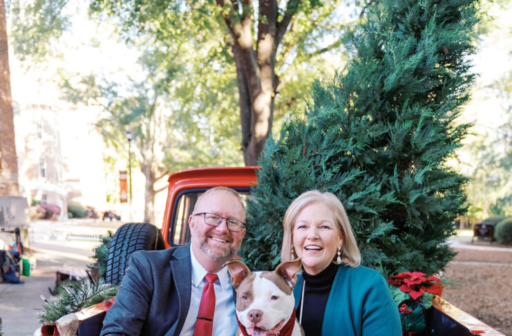 Jason Elkins and Mercer President Dr. Penny L. Elkins sit with a dog in the back of a red truck decorated with Christmas trees and blankets.