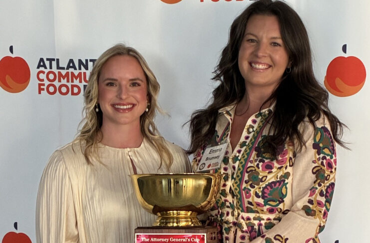 Two women holding a gold trophy with a plaque, standing in front of an Atlanta Community Food Bank banner.