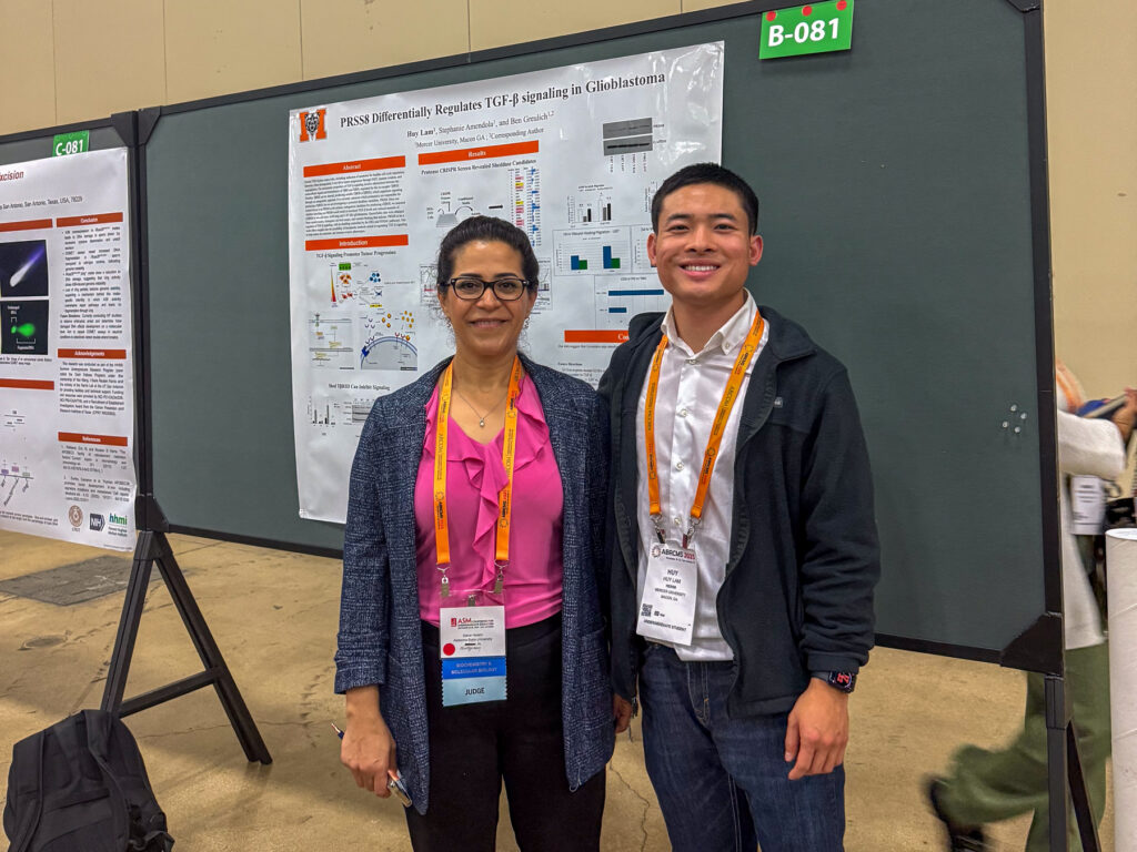Dr. Sahar Hasim and Huy Lam standing and smiling in front of a scientific research poster at a conference.