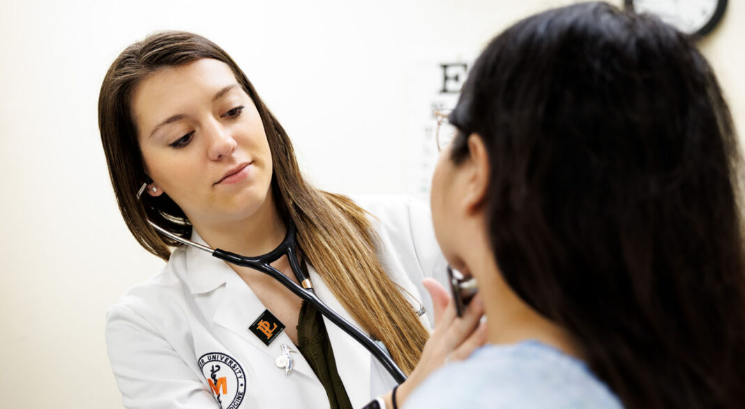 A healthcare professional uses a stethoscope to examine a patient in a medical office.