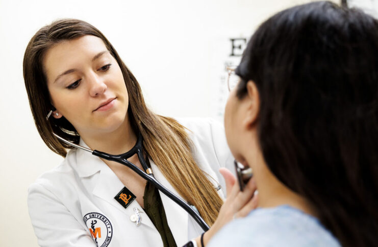 A healthcare professional uses a stethoscope to examine a patient in a medical office.