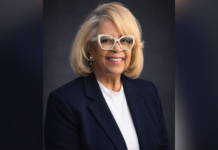 80-year-old works toward another milestone: A Mercer degree Smiling woman with blond hair, glasses, and black blazer poses against a dark background.