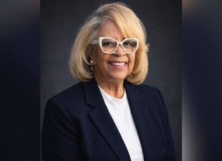 80-year-old works toward another milestone: A Mercer degree Smiling woman with blond hair, glasses, and black blazer poses against a dark background.