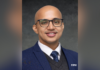 Dr.P.H. student selected for global health fellowship, public health think tank A man with glasses, a blue suit, and a polka dot tie smiles at the camera against a dark gray background.