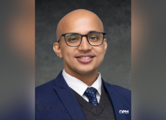 Dr.P.H. student selected for global health fellowship, public health think tank A man with glasses, a blue suit, and a polka dot tie smiles at the camera against a dark gray background.