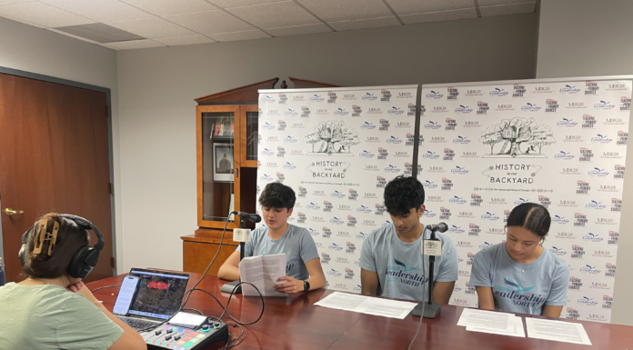 Podcast explores Georgia’s role in Revolutionary War Three teenagers read scripts at a table while a person records audio using a laptop and mixer in a small studio.