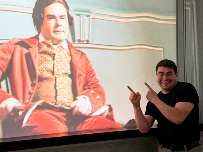 kitchens edit Smiling man points at a projected image of an actor in historical costume on a screen.