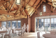 Building for BEARS: New student center to elevate Mercer’s Macon campus Architectural rendering of a dining hall with wooden beams, brick walls, large windows, and round tables with chairs.