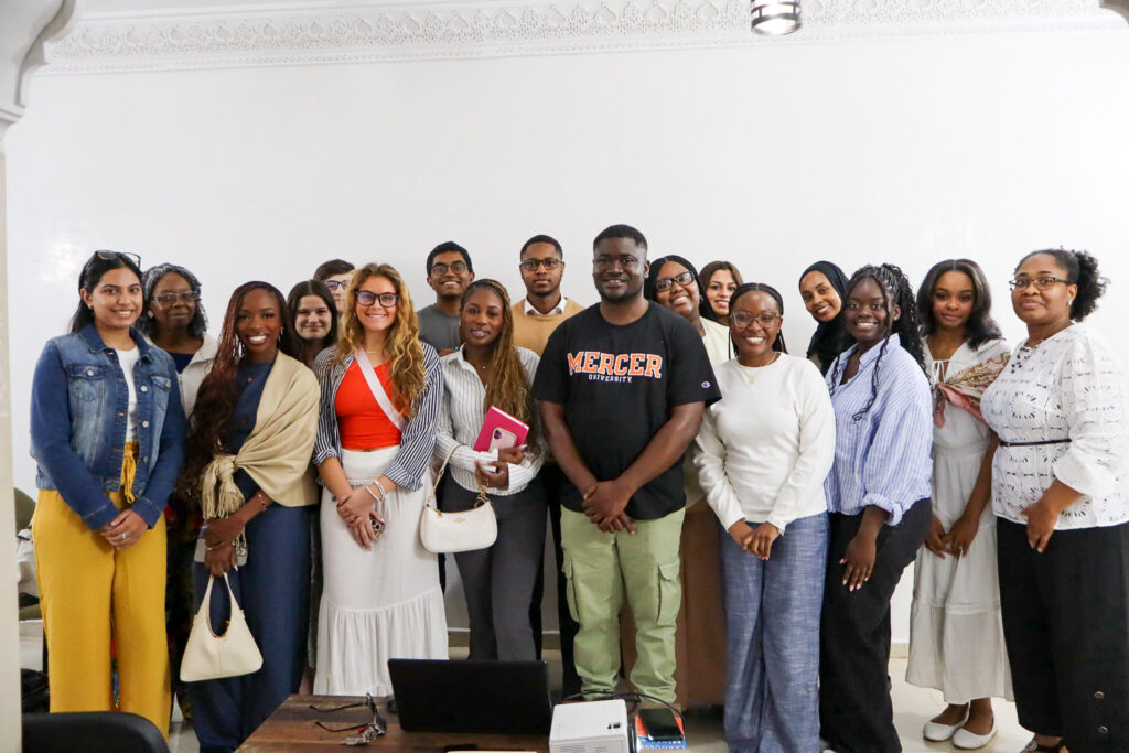 A group of people pose together indoors, standing in front of a white wall and smiling at the camera.