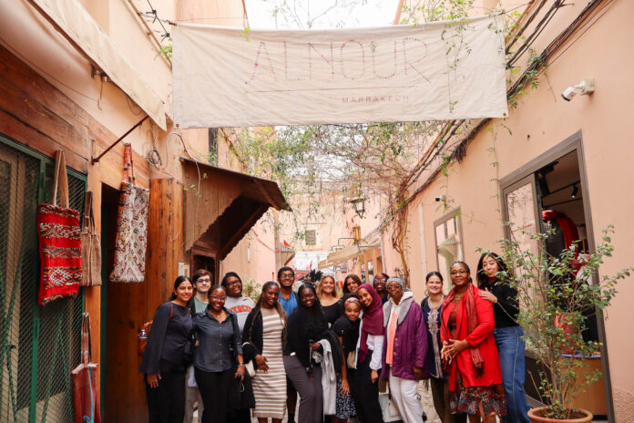 A group of people pose together in an outdoor hallway beneath a large banner reading Alnour Marrakech.